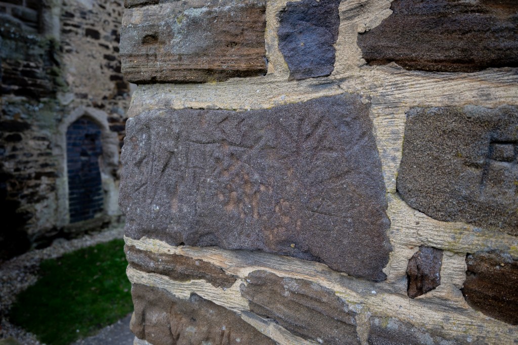 The corner of an entrance into the church. On a large rectangular grey stone, lines, zigzags, diamonds and V shaped have been drawn. On a separate stone a P has been carved. 