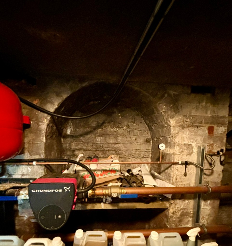 In the background a bricked up archway which now has a red boiler and pipes going in front of it. 