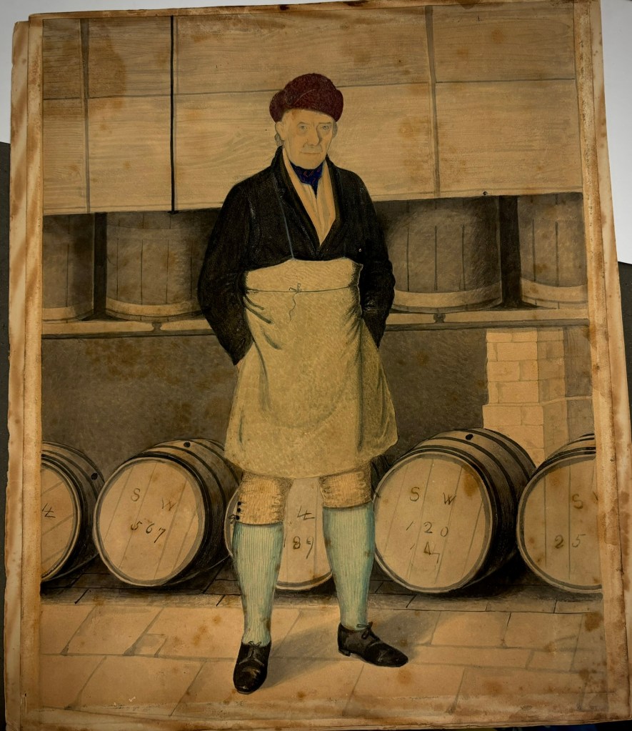 A man in 18th century dress and apron with a russet coloured hat and indigo neckerchief. He has blue eyes and white hair. He is standing in front of beer barrels marked SW