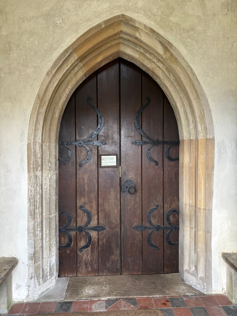 A large arched shaped heavy wooden door with great iron work hinges and a large iron ring knocker.