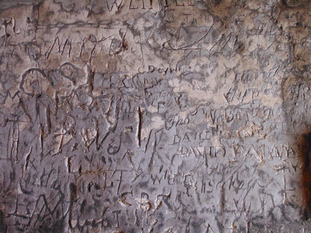 A chalk wall covered in letters and initials and shapes. 