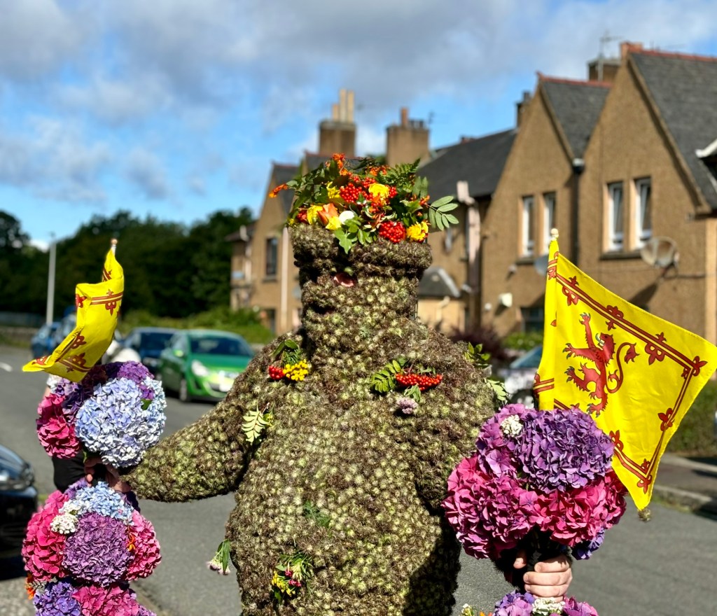 A close up of the Burryman with his flowery staffs and flags standing outside some houses. 