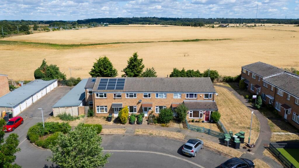A picture taken with a drone showing terraces of 1970s houses with a wide stretch of golden fields behind and in the distance the darrk trees a low hills of the green sand ridge at Sandy.