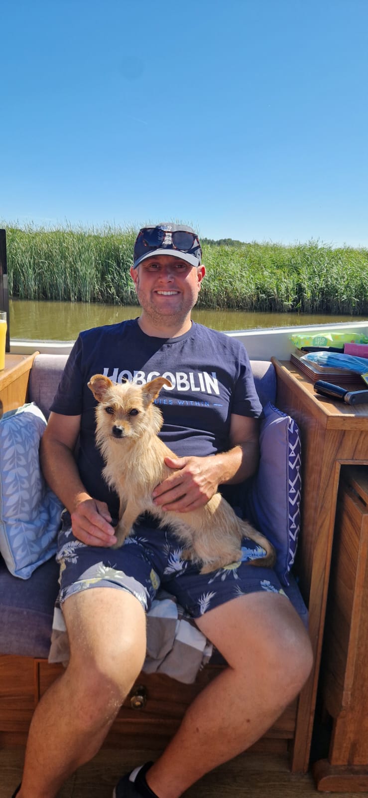 A man wearing a baseball cap is sitting on a boat holding Dolly the caramel coloured chihuahua