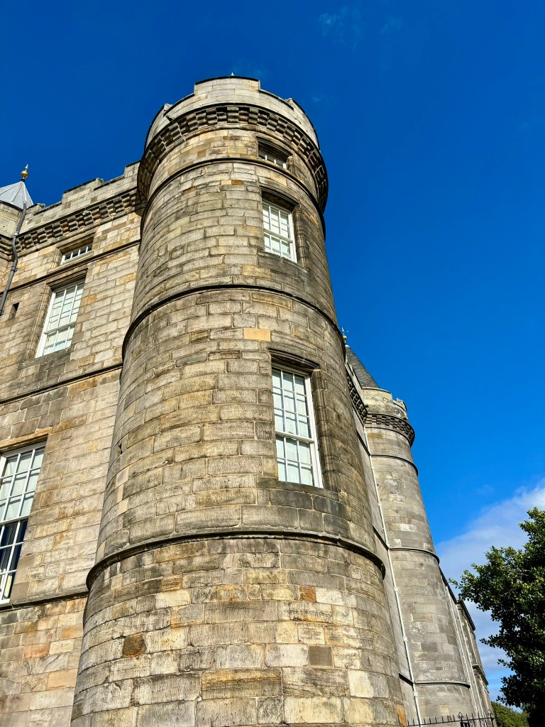 A round tower of a castle with narrow windows and bright blue sky behind it. 