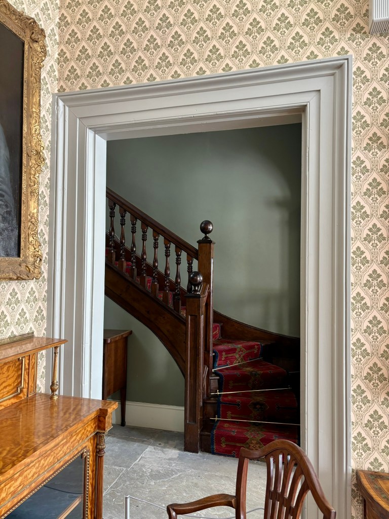 A doorway leading to old stairs with a red patterned carpet and dark wood banister. 