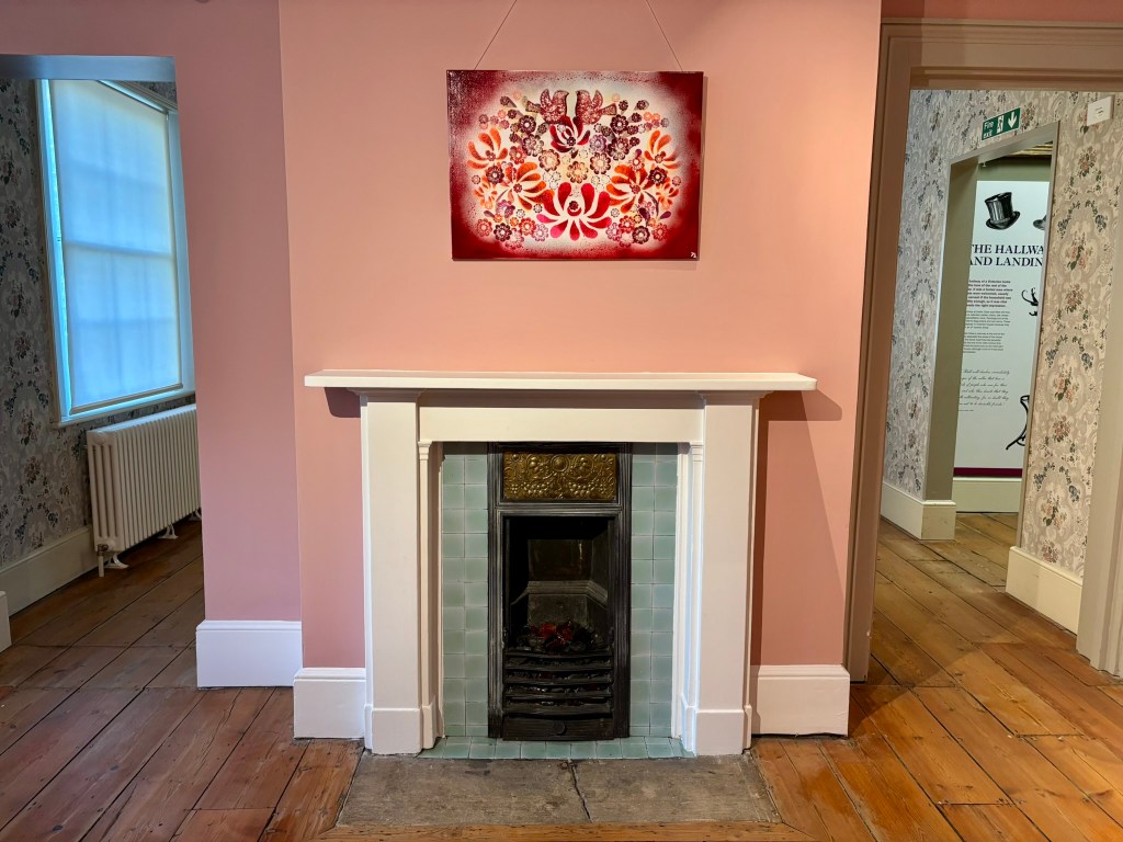 A pink wall with a fireplace in it. The fireplace has pale blue tiles and white mantlepiece.