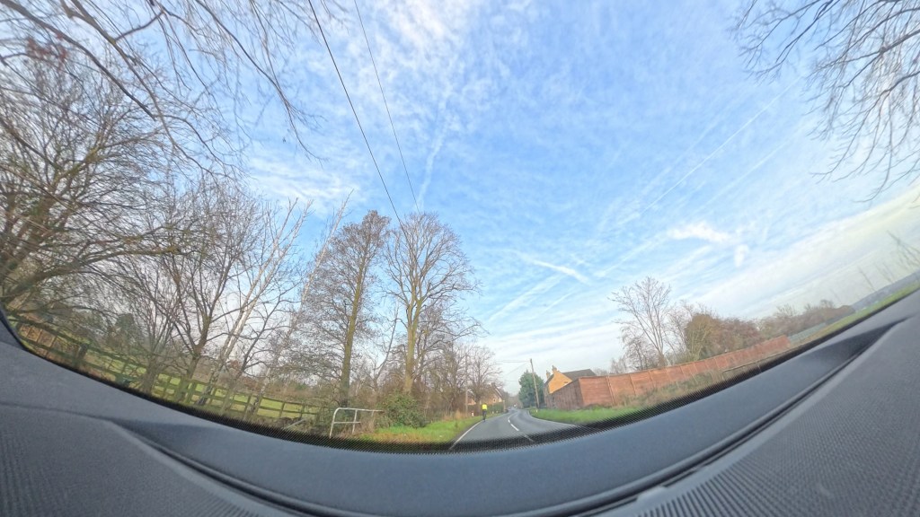Dash cam image of straight road and a cyclist in fluorescent yellow ahead. There are winter trees and a house at the side of the road