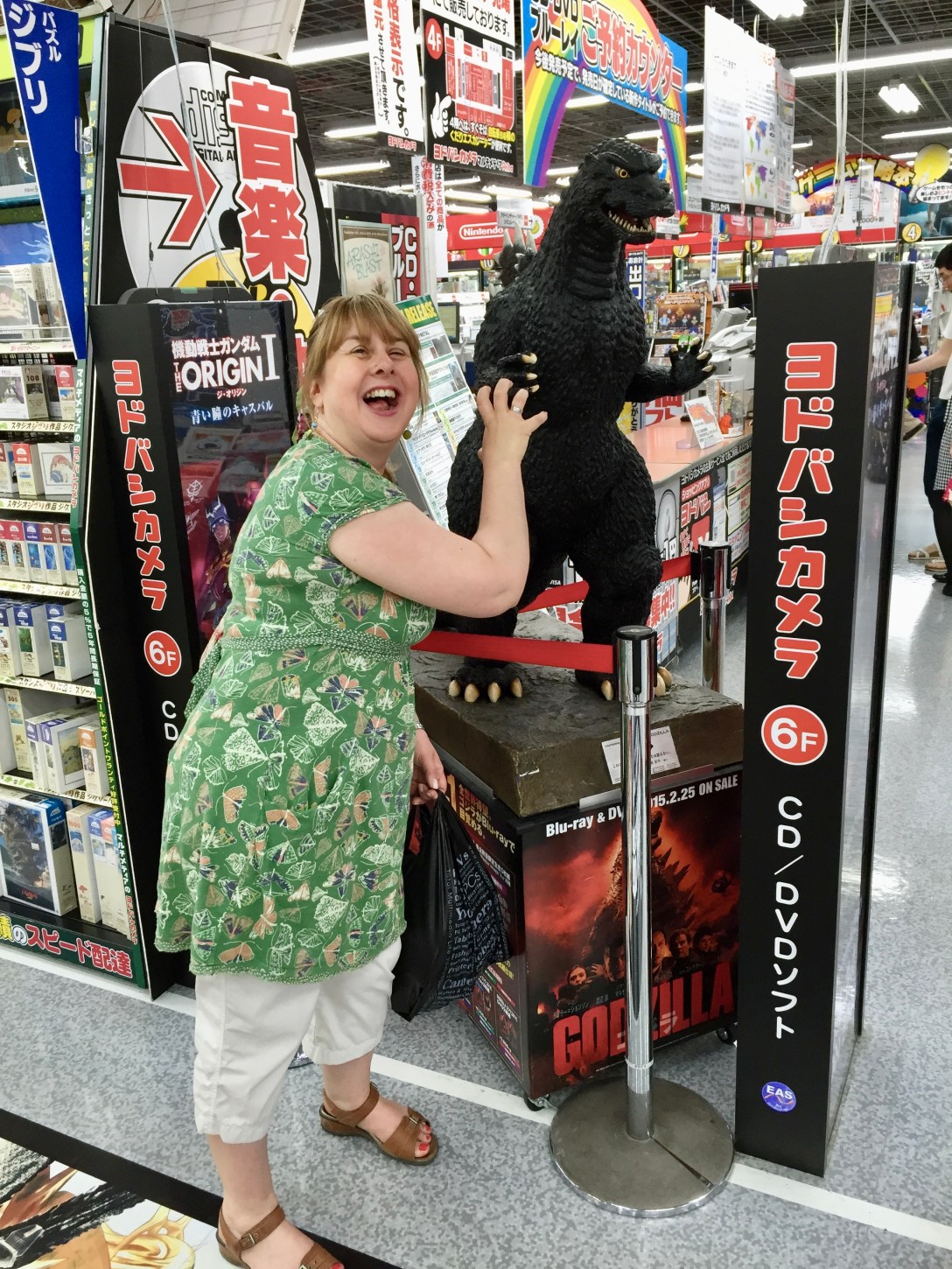 me standing in a Japanese shop next to Godzilla I am making my hand into a claw and pulling a growling face