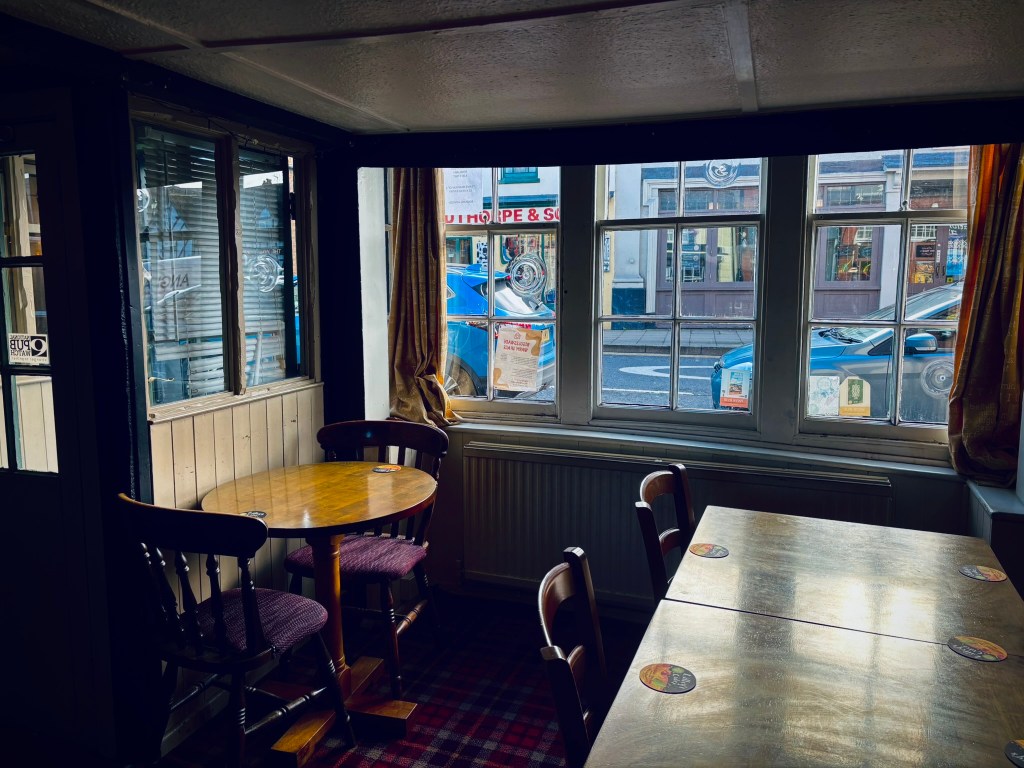A window onto the high street with a round table and larger table in front of it inside the pub. 