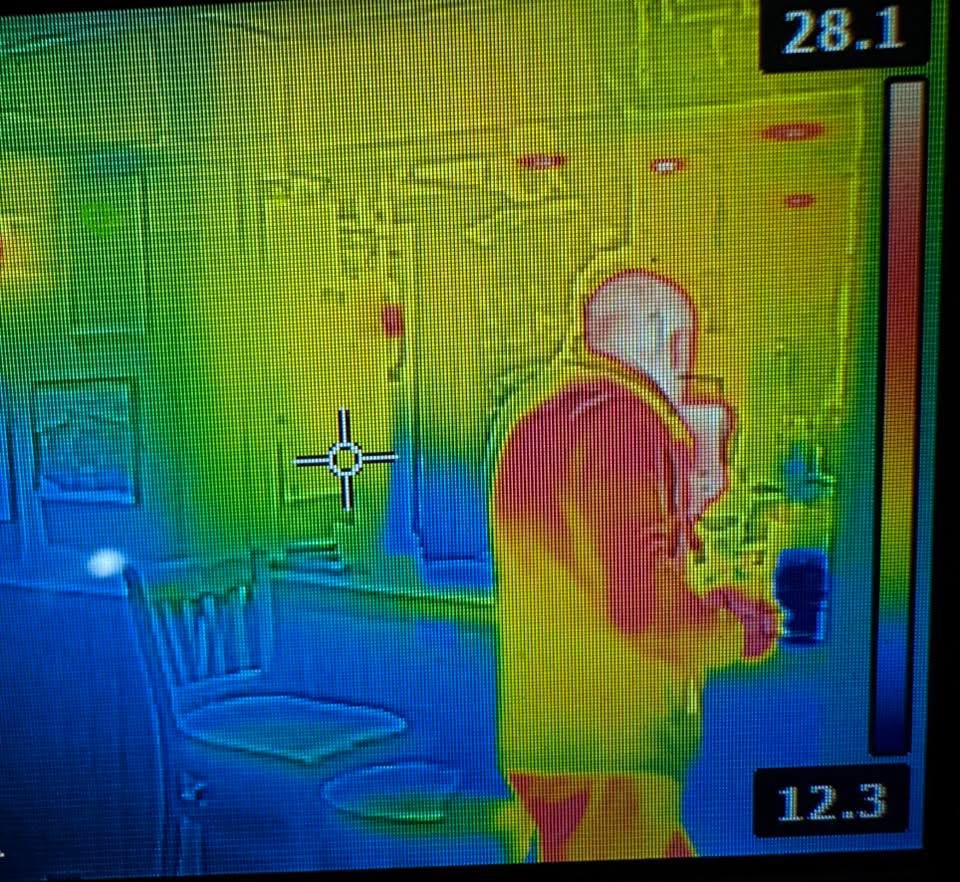 A thermal image showing a man at the bar with his phone. He has his back to us and his head is white showing he is warm. The bottom of the image is blue showing the bar is cold. 
