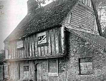 A black and white photo of an old medieval building with wood beams and over hanging first floor. 