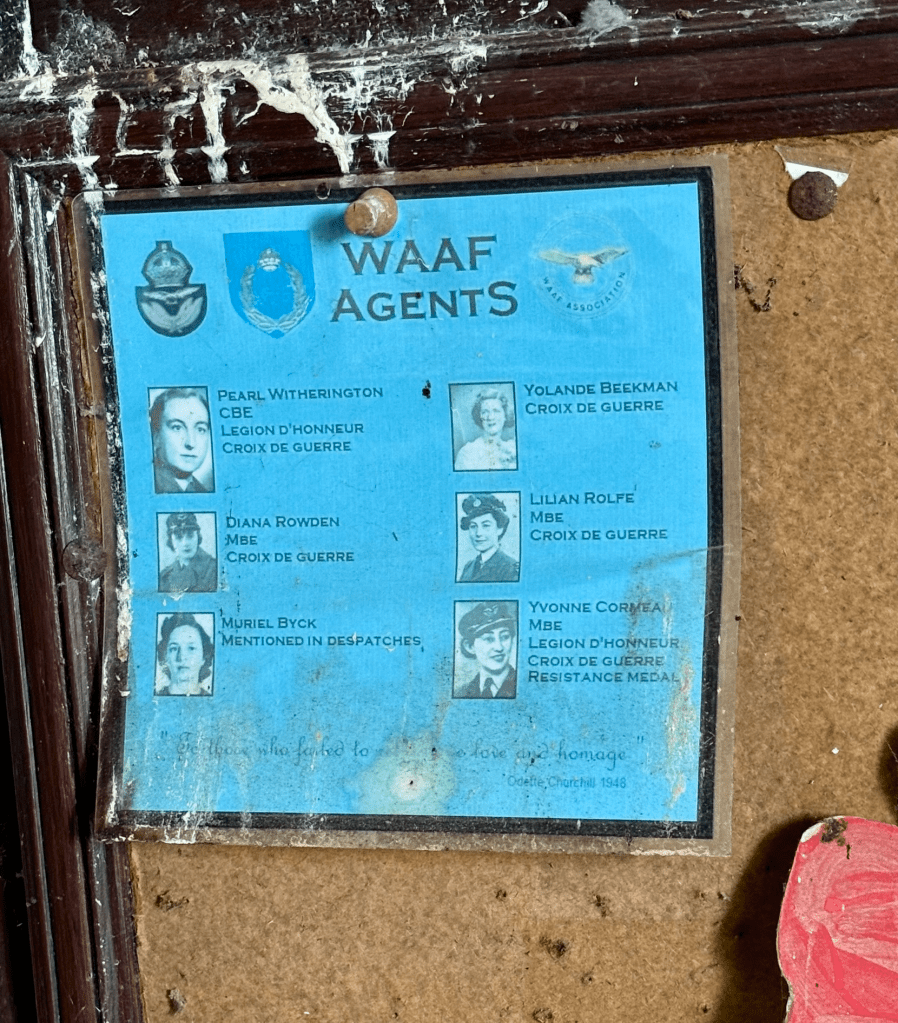 A faded blue poster on a dusty cork board. The blue poster says WAAF AENTS at the top. There are 6 photos of women with the names next to them: Pearl Witherington is the first the others are Diana Rowden, Muriel Byk, Yolande Beekman Lilian Rolfe and Yvonne Cormea