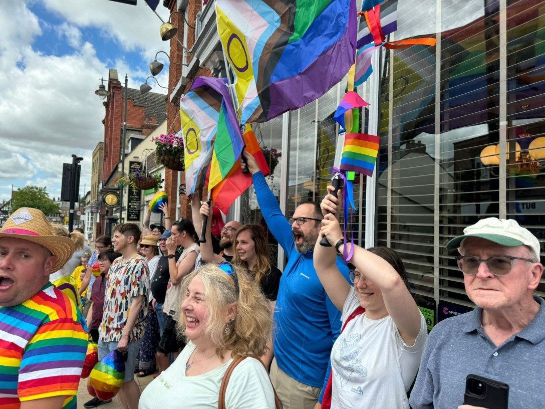 A group of brightly dressed people waving pride flags on a street