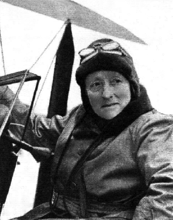 The flying Duchess wearing flying hat and goggles on her head, sitting in an aeroplane. She is looking to the side and is clearly an older lady. 