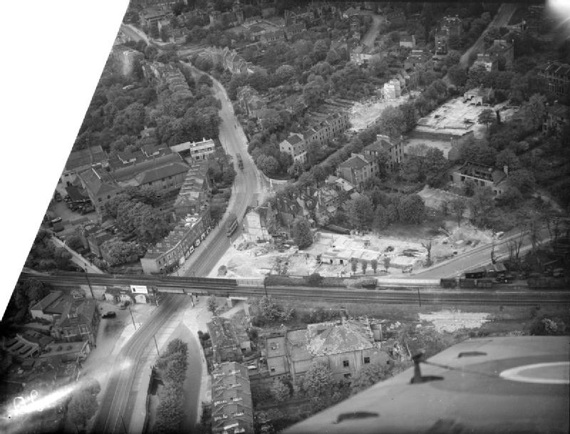 An aerial black and white shot of streets some of which are scarred with pale areas of destruction, there are many trees